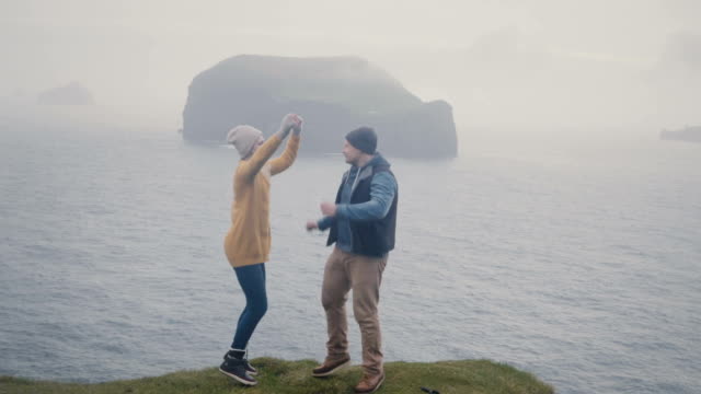 Young-stylish-couple-having-fun-together.-Man-and-woman-dancing-on-the-shore-of-the-sea-in-foggy-day