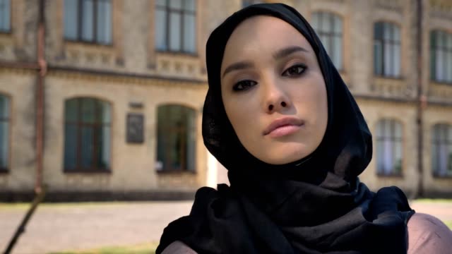Tagsüber-im-Sommer,-schaut-aufbauend-auf-Hintergrund,-religiöse-Konzept-junge-selbstbewusstes-muslimische-Mädchen-in-die-Kamera
