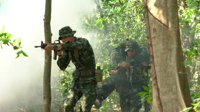Soldier-holding-gun-weapon-and-waring-armor-uniform-with-smoke.-Soldiers-are-taking-the-wounded-man-out-of-the-jungle.