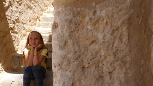 Girl-sitting-on-stairs-at-beige-stone-steps-and-thinking
