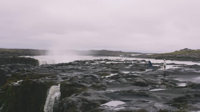 Junge-Hipster-paar-Strandung-in-der-Nähe-des-mächtige-Wasserfalls-in-Island-und-die-Aussicht-genießen