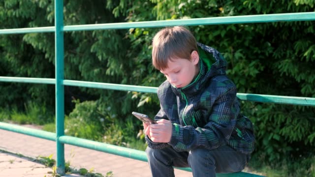Junge-Ruft-das-Telefon-und-sprechen,-sitzen-im-Park.
