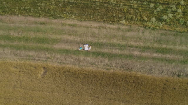 Young-little-cute-girls-Playing-explorers-with-Map-of-Italy-reading-and-pointing-in-green-wheat-Field-slow-motion-drone-top-aerial-view