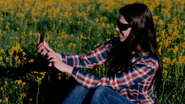 Frau-macht-eine-Selfie-am-Telefon-sitzen-auf-dem-Rasen-unter-den-gelben-Blumen.