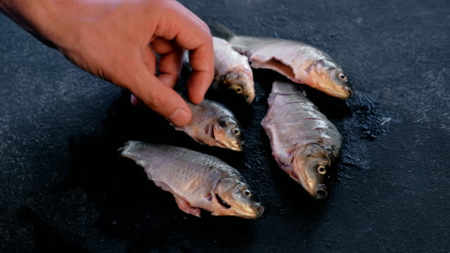 Man-plays-with-fresh-clean-carp-fish-on-black-table.-Cooking-fish.-Close-up-hand.