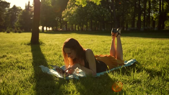 Girl-sitting-in-the-park-among-the-trees-and-use-the-Internet-on-tablet
