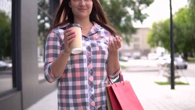 The-girl-goes-after-shopping-with-bags-in-her-hands-drinking-coffee.-4K