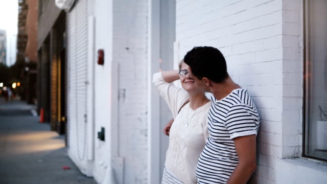 Happy-young-authentic-romantic-couple-stand-close-together-on-a-date-by-white-building-wall-in-evening-Soho,-New-York