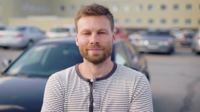 Portrait-of-a-successful-man-standing-by-his-car-on-the-outside-parking-lot-and-smiling