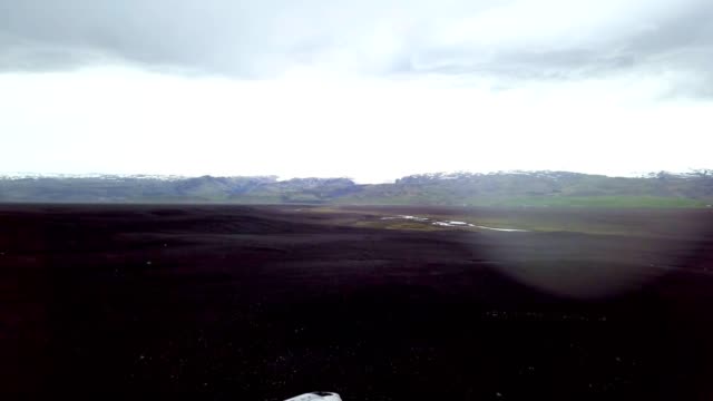 Drone-Ansicht-Antenne-des-jungen-Mannes-steht-auf-Flugzeug-stürzte-am-schwarzen-Sandstrand,-schaut-sich-um-ihre-Betrachtung-Umgebung-Sehenswürdigkeit-zu-besuchen-in-Island-und-stellen-mit-dem-Wrack---4K-Auflösung-ausgestreckte-Armen