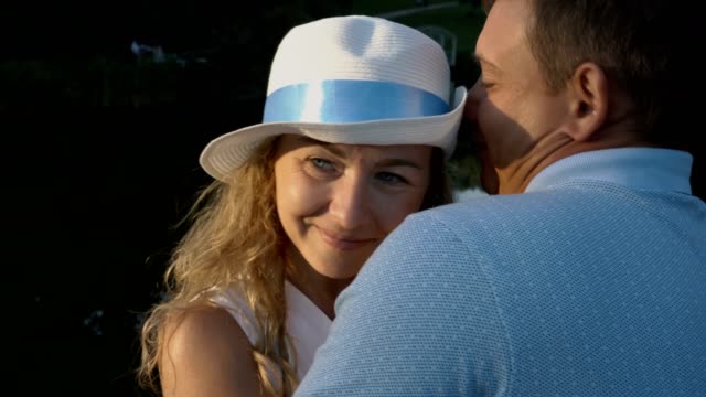 Close---up-of-a-couple-in-love.-Happy-girl-in-white-hat-at-sunset-hugs-and-kisses-with-a-man-in-the-Park-on-the-pond-background.