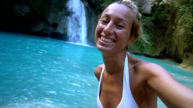 Young-woman-taking-selfie-portrait-with-a-beautiful-waterfall-on-the-Cebu-Island-in-the-Philippines.-People-travel-nature-selfie-concept.-One-person-only-enjoying-outdoors-and-tranquillity-in-a-peaceful-environment--4K-video