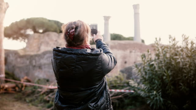 Rückansicht-des-glücklich-senior-lächelnde-Frau-kaukasischen-Aufnahme-eines-Smartphone-Fotos-von-antiken-Ruinen-in-Ostia,-Italien-im-Urlaub