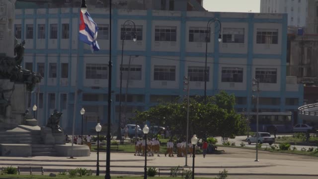 cuban-school-kids-in-everyday-life-in-old-Havana,-cuban-flag-on-public-square
