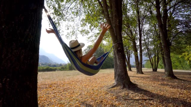Happy-young-woman-on-hammock-swinging-at-sunset-legs-up-having-fun-and-enjoying-freedom-in-nature--late-Summer-days.-People-travel-joy-concept