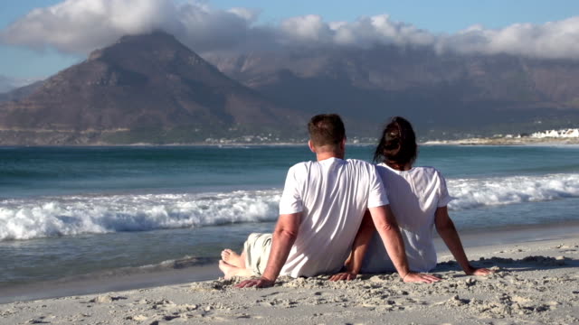 Couple-sitting-close-together-on-beach-and-enjoying-the-view,South-Africa
