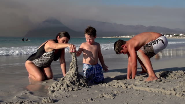 Mutter-mit-zwei-Kinder-spielen-mit-sand-am-Strand,-Cape-Town