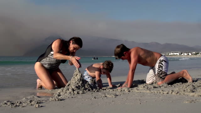 Madre-con-dos-niños-jugando-en-la-arena-en-la-playa,-Cape-Town