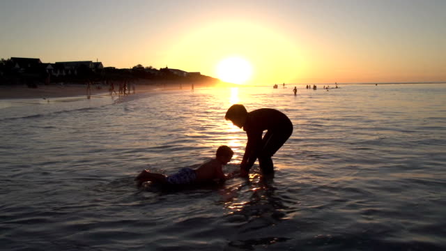 Dos-chicos-jugando-en-la-playa-en-silueta-al-atardecer,-ciudad-del-cabo