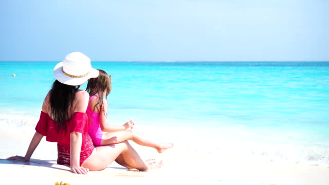 Little-adorable-girl-and-young-mother-at-tropical-beach-enjoy-their-sea-vacation