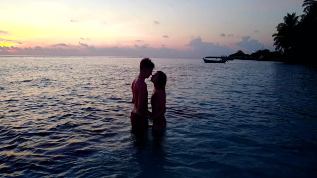 v04152-fliegenden-Drohne-Luftaufnahme-der-Malediven-weißen-Sandstrand-2-Menschen-junges-Paar-Mann-Frau-romantische-Liebe-Sonnenuntergang-Sonnenaufgang-auf-sonnigen-tropischen-Inselparadies-mit-Aqua-blau-Himmel-Meer-Wasser-Ozean-4k
