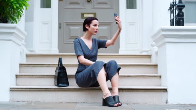 Stilvolle-Frau-sitzen-auf-Stufen-des-Gebäudes-nehmen-Selfie