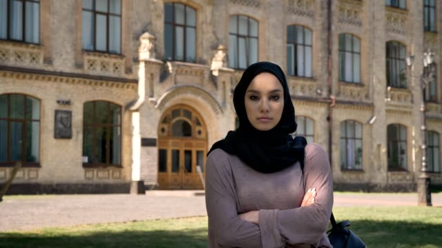 Selbstbewusstes-muslimische-Mädchen-steht-mit-verschränkten-tagsüber-im-Sommer,-gerade-in-die-Kamera,-aufbauend-auf-Hintergrund,-religiöse-Konzept