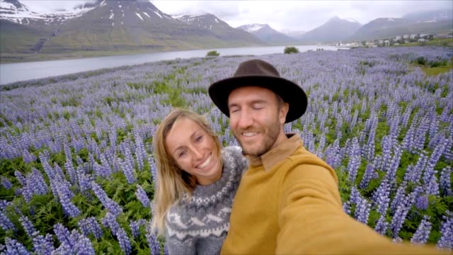 Slow-motion-video-de-pareja-de-jóvenes-teniendo-selfie-retratos-en-el-campo-de-la-flor-de-color-púrpura-en-Islandia-cerca-de-lago-y-montañas-feliz-gente-viaje-amor-concepto