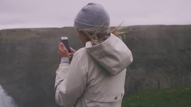 Joven-touristtaking-pucture-con-smartphone-de-cascada-en-Islandia,-cardán-tiros,-cámara-lenta