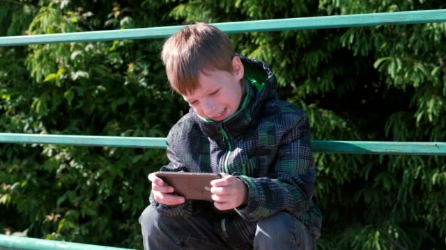 The-boy-plays-a-game-on-his-mobile-phone-while-sitting-in-the-Park.