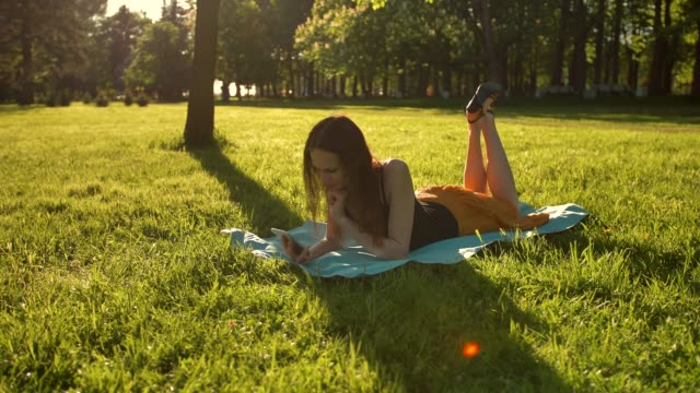 Female-laying-down-over-green-grass-while-typing-a-message-on-phone