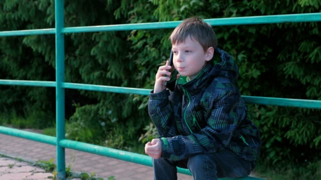 Junge-Ruft-das-Telefon-und-sprechen,-sitzen-im-Park.
