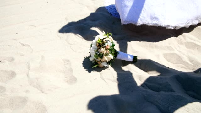 summer,-desert,-against-the-background-of-sand,-and-the-wedding-bouquet-lying-on-it,-shadows,-outlines-of-people-in-wedding-dresses,-join-hands