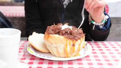 Tourist-girl-eating-a-Goulash-in-a-bread-bowl-at-christmas-annual-market-in-Budapest.-Tourist-enjoying-and-tasting-traditional-hungarian-cuisine