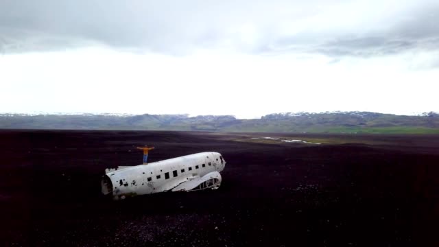 Drone-vista-aérea-de-joven-está-parado-brazos-extendidos-en-avión-que-se-estrelló-en-la-playa-de-arena-negra-mirando-su-lugar-famoso-de-contemplar-un-entorno-para-visitar-en-Islandia-y-posan-con-el-naufragio---4K-de-resolución