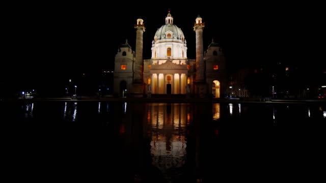 eine-extrem-breite-Nachtaufnahme-St-Charles-Kirche-spiegelt-sich-in-einem-Pool-in-Wien