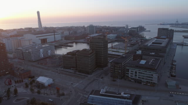 Aerial-view-of-Malmö-cityscape-at-sunset.-Drone-shot-flying-over-city-street,-buildings-and-construction-site-at-dusk.-Business-office-buildings,-tower-cranes-and-sea-coast,-Sweden