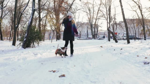 Young-woman-playing-with-Jack-Russell-terrier-in-winter-time-through-park,-dolly-shot