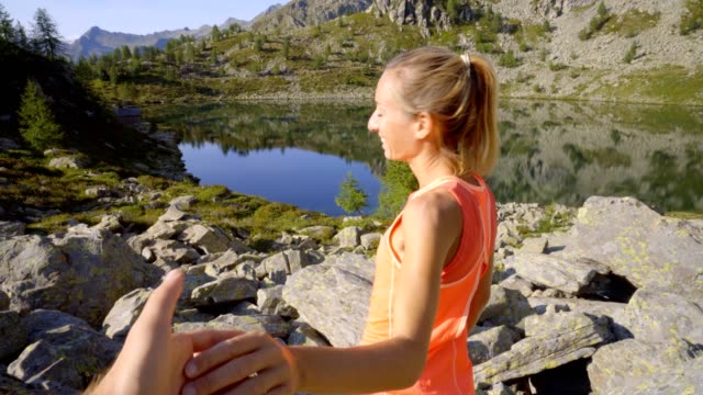 Follow-me-to-the-beautiful-nature,-woman-hiking-leading-boyfriend-to-mountain-lake.-Follow-me-to-concept.-Female-holding-male-hand-leading-him-to-mountain-lake.-Following-point-of-view