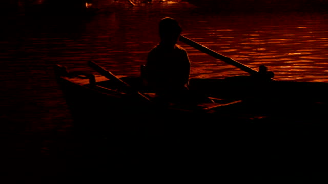 Junge-in-einem-Boot,-beleuchtet-von-der-Ghats-am-Ganges:--Varanasi,-Indien