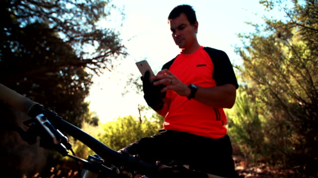 Mountainbiker-sitzt-auf-Fahrrad,-die-in-seinem-Smartphone