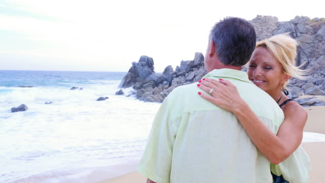 An-older-woman-smiling-and-whispering-"I-love-you"-into-her-husband's-ear-at-the-beach