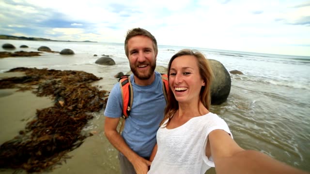 Young-couple-stand-near-Moeraki-boulders-and-take-selfie-portrait