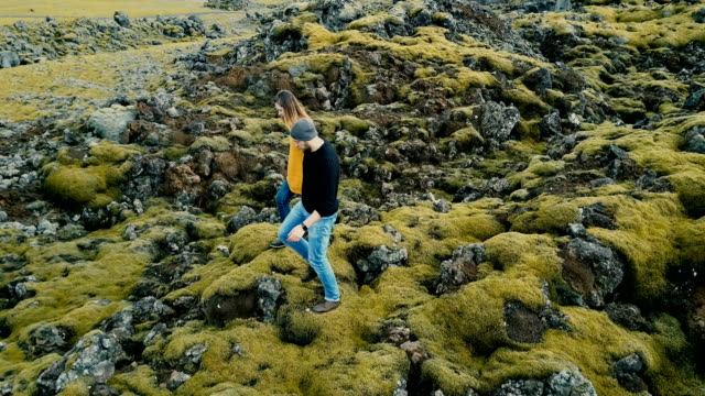 Vista-aérea-de-la-joven-pareja-elegante-paseando-por-el-campo-de-lava-volcánica-en-Islandia.-Hombre-y-la-mujer-van-a-su-coche
