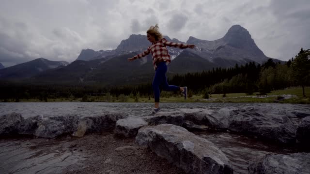 Young-woman-jumps-rock-to-rock-on-mountain-lake