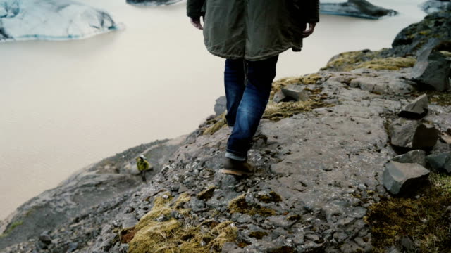 Hombre-guapo-joven-paseando-por-las-rocas-en-la-montaña-cerca-de-la-laguna-de-hielo-Vatnajokull-en-Islandia