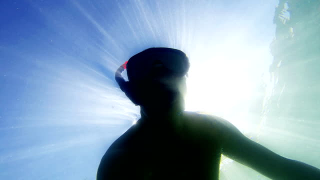 Young-man-snorkeling-with-sunrays-view-from-bellow,-uhd-shoot