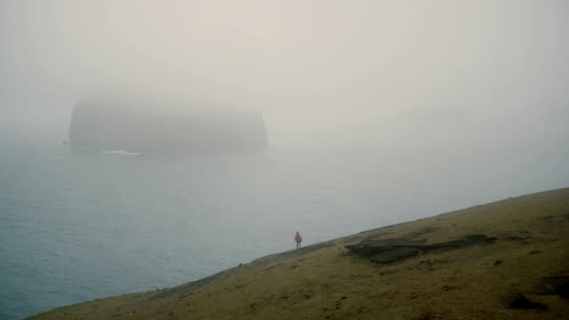 Junge-Reisende-zu-Fuß-am-Ufer-des-Meeres-in-Nebel-und-Strand-im-bewölkten-Tag-in-Island-in-der-Nähe-von-Vestmannaeyjar-erkunden