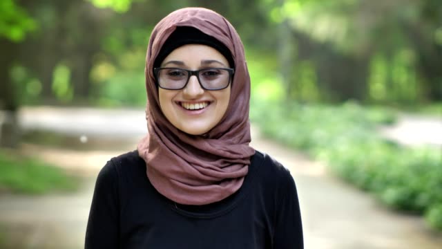 Retrato-de-una-joven-sonriente-en-gafas-llevar-hijab,-al-aire-libre,-en-un-parque-en-el-fondo.-50-fps