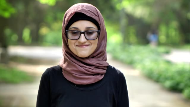 Portrait-of-a-young-smiling-girl-in-glasses-wearing-hijab,-outdoor,-in-a-park-in-the-background.-50-fps